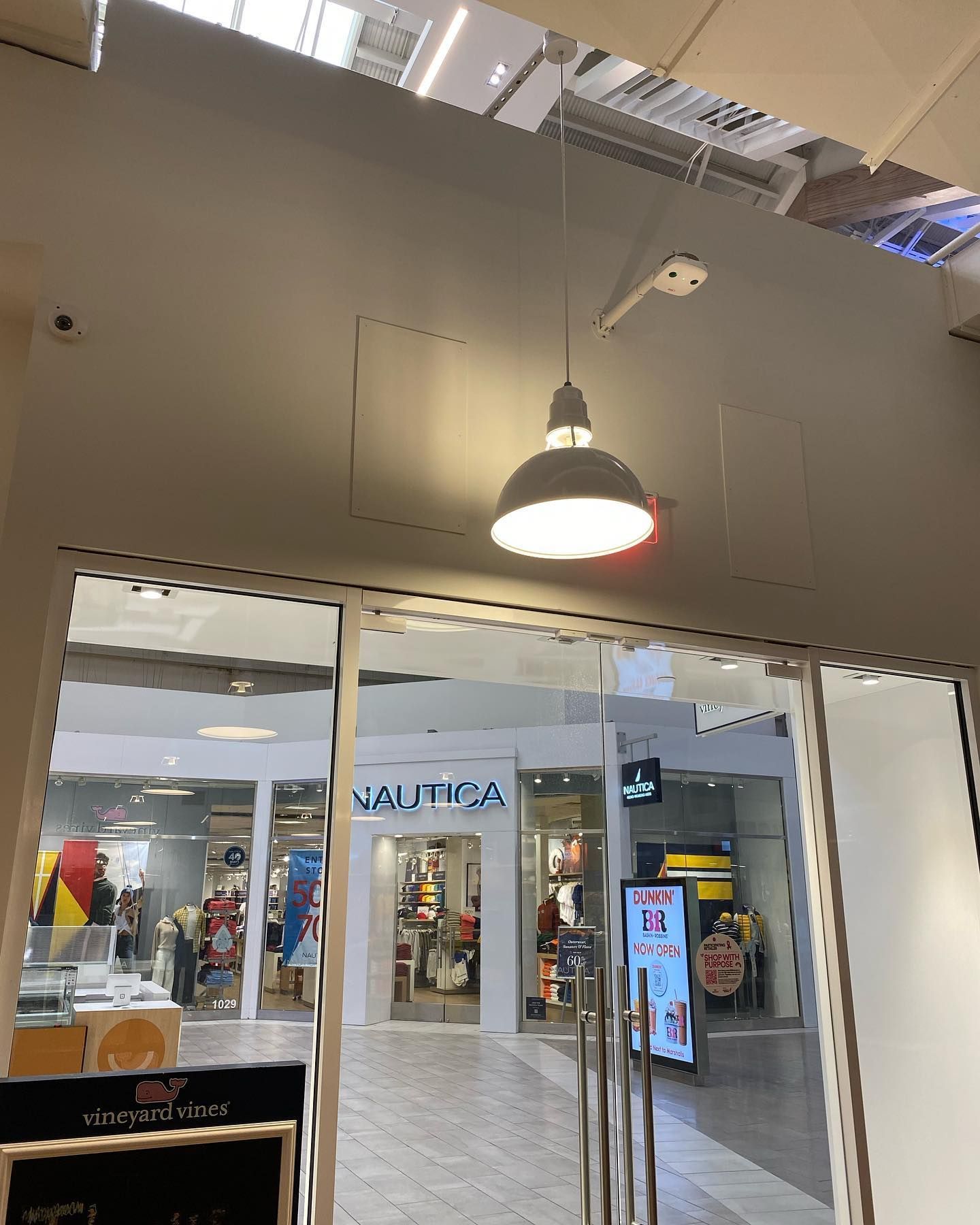 View through an entrance of a store, showing stores, including Nautica. A hanging lamp illuminates the entry.