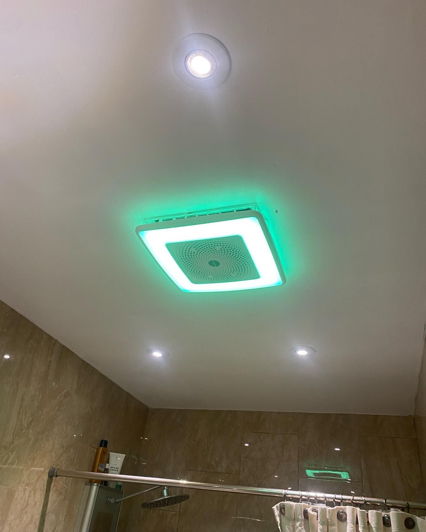 Green-lit ceiling fan in a bathroom with tan walls and recessed lighting.