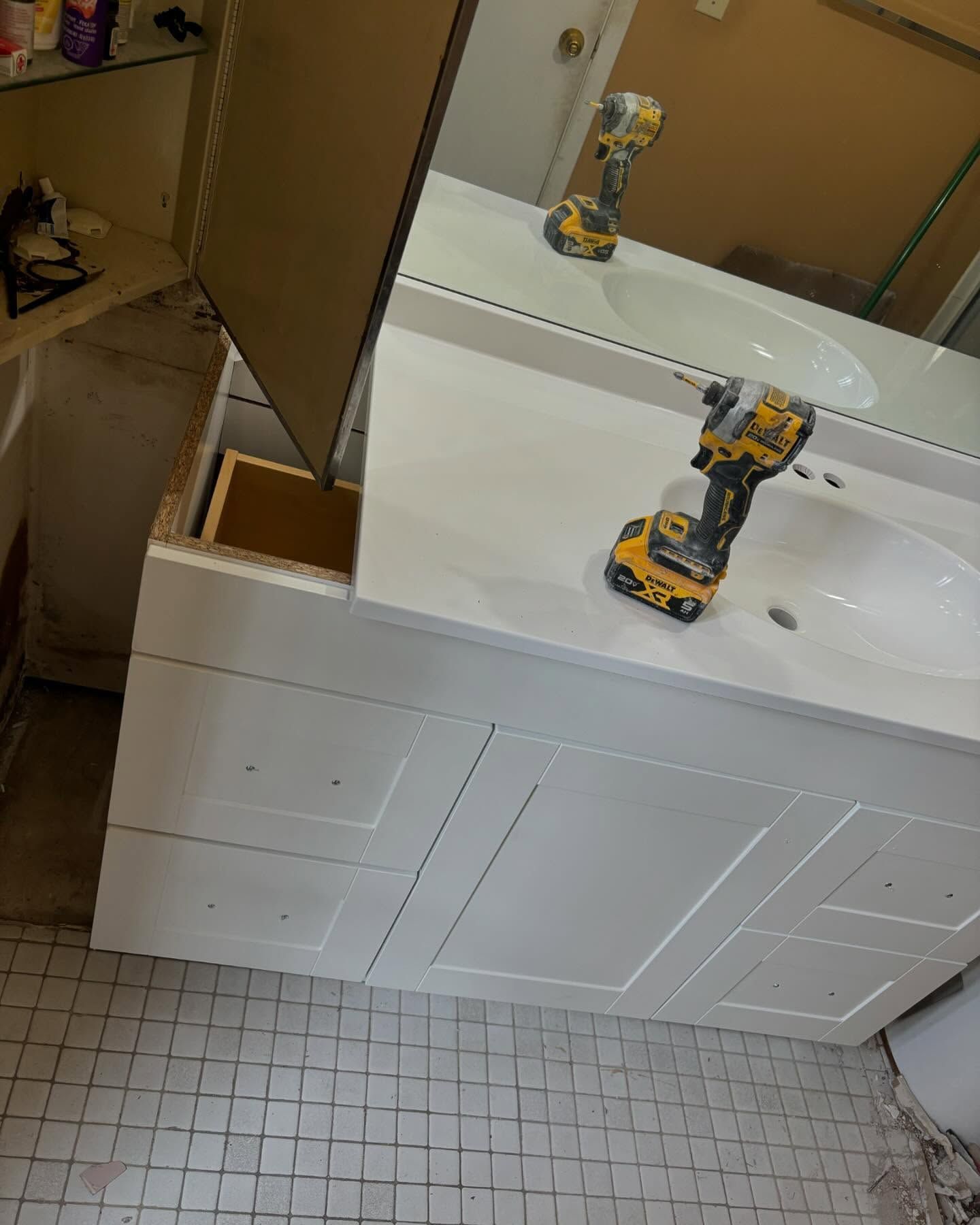 White bathroom vanity with a mirror, a drill, and a partially open cabinet.