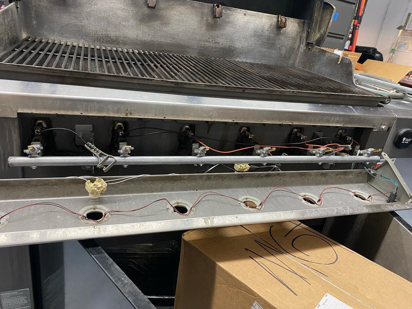 Stainless steel grill interior; burners and wiring visible, grill grate above.