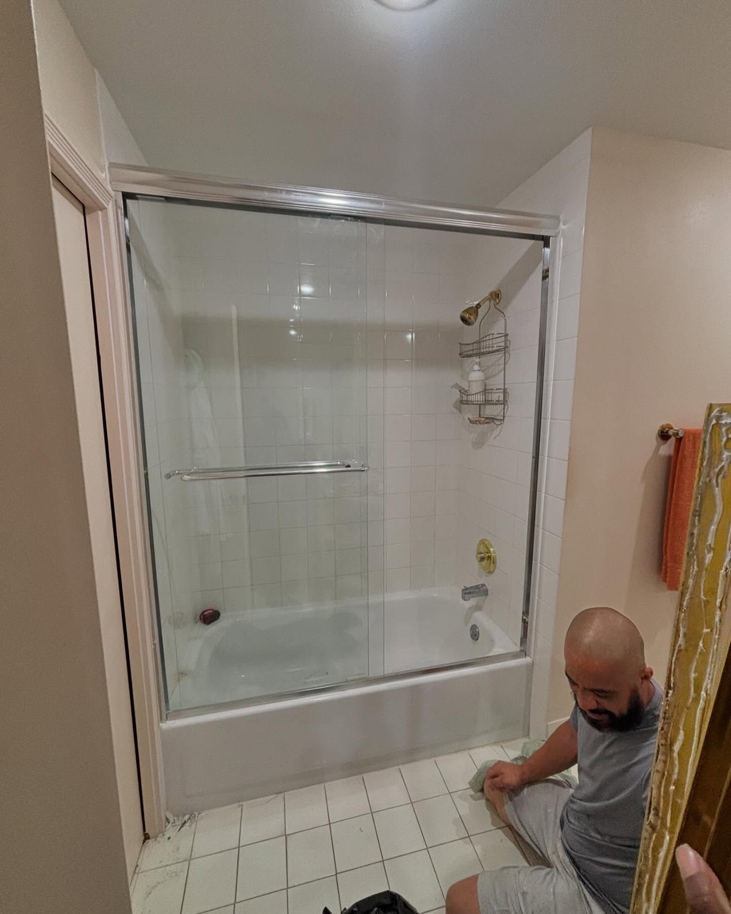 Man installing shower door in bathroom with white tiles and walls.