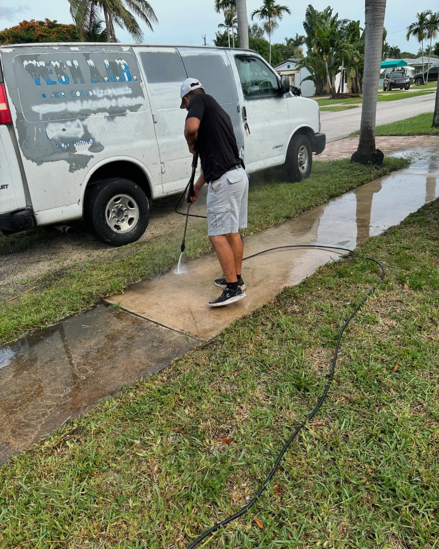 Man pressure washing a sidewalk next to a white van, in a residential area.