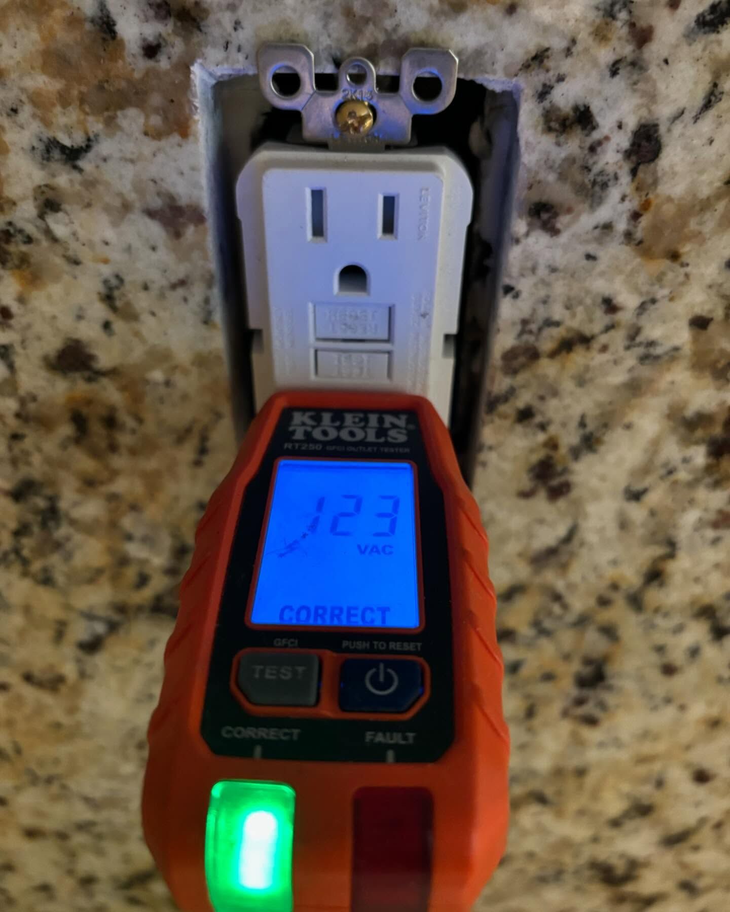 Outlet tester plugged into electrical outlet, reading 123 volts. Green light indicates correct wiring.