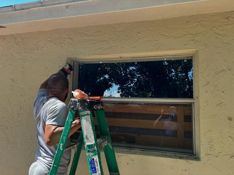Man on ladder, removing or installing window, exterior wall, sunny day.
