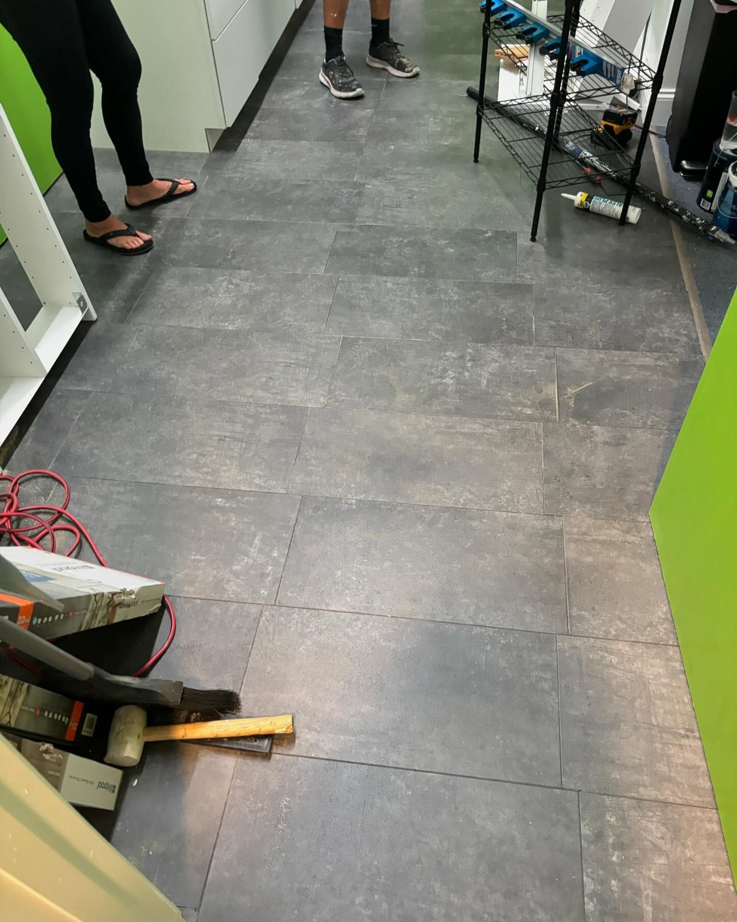 Gray interlocking floor tiles in a narrow hallway. People and tools are present.
