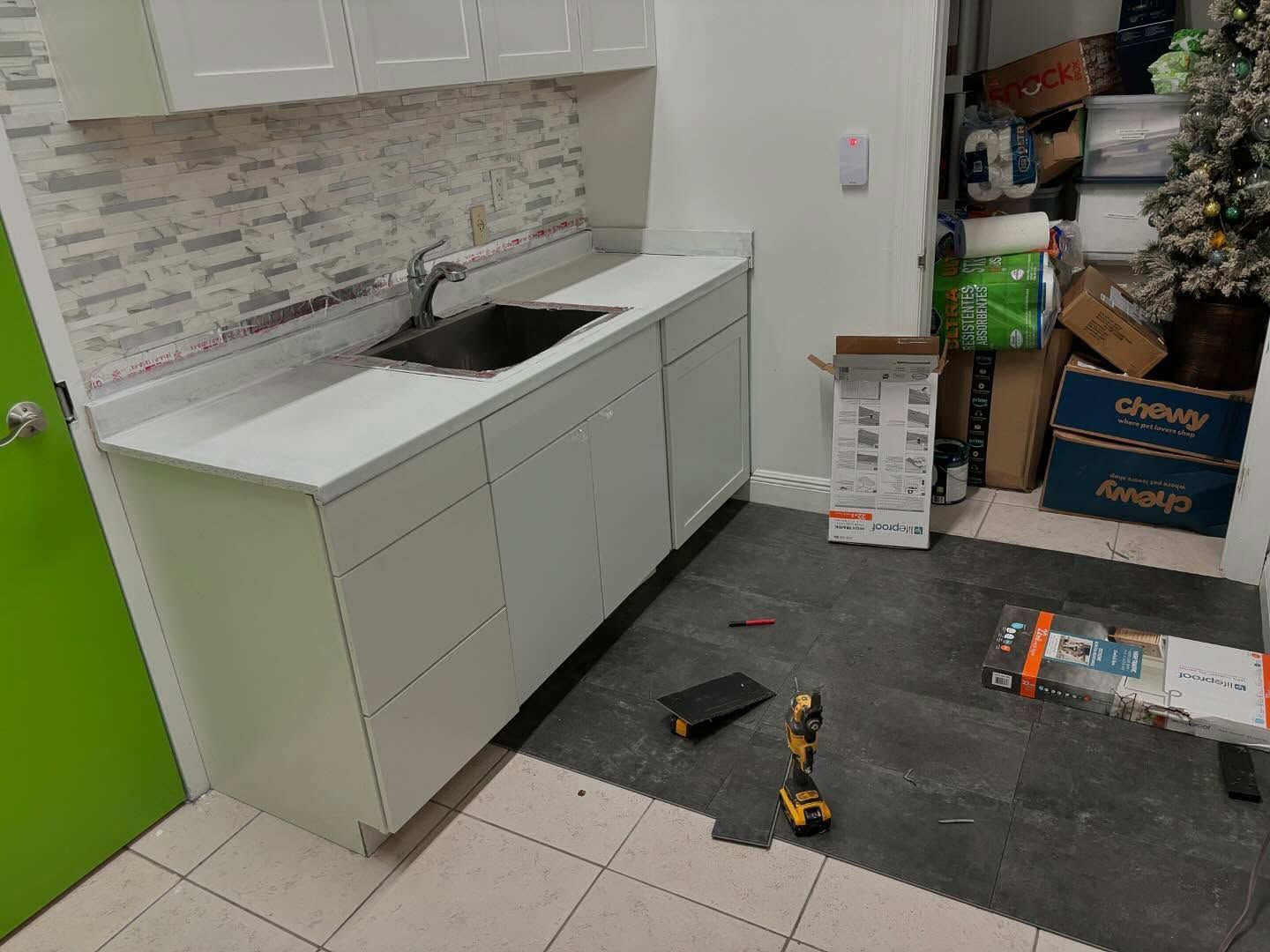 Kitchen with white cabinets, sink, and countertops. A cluttered storage area is visible on the right.