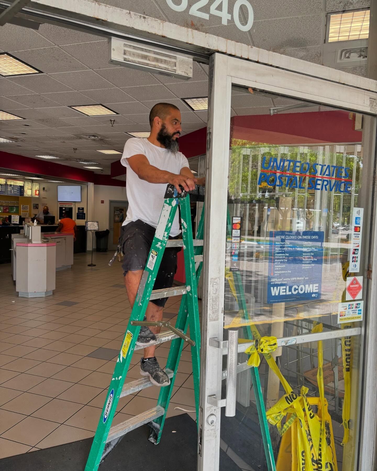 Man on ladder working on the door frame of a store with red and white decor.