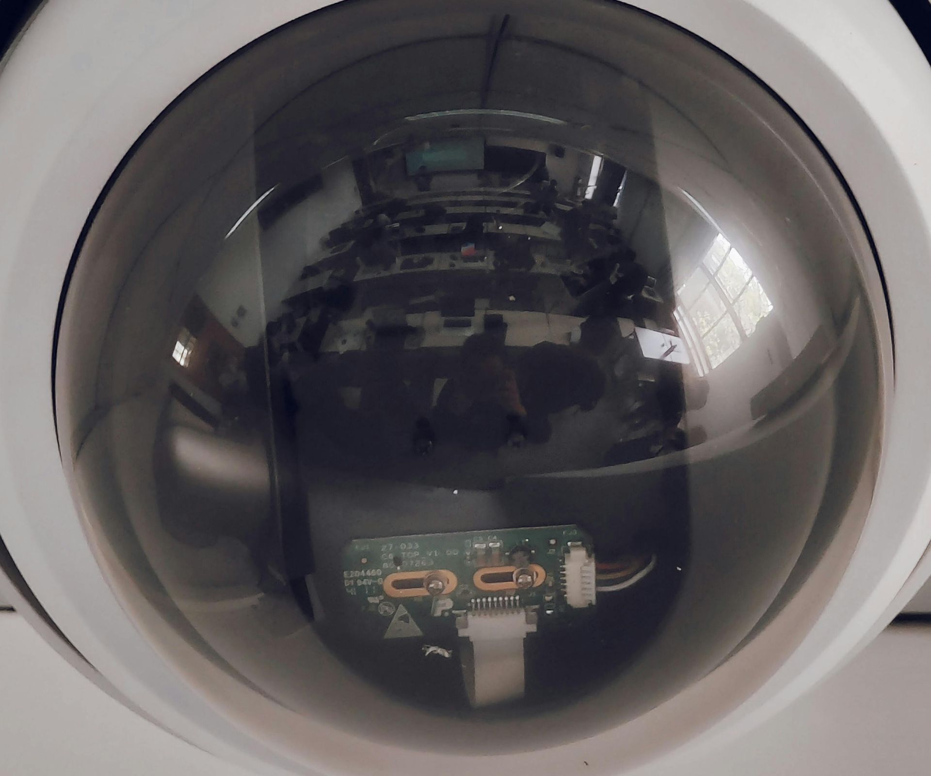 Domed security camera view reflecting a room with equipment and a green circuit board below