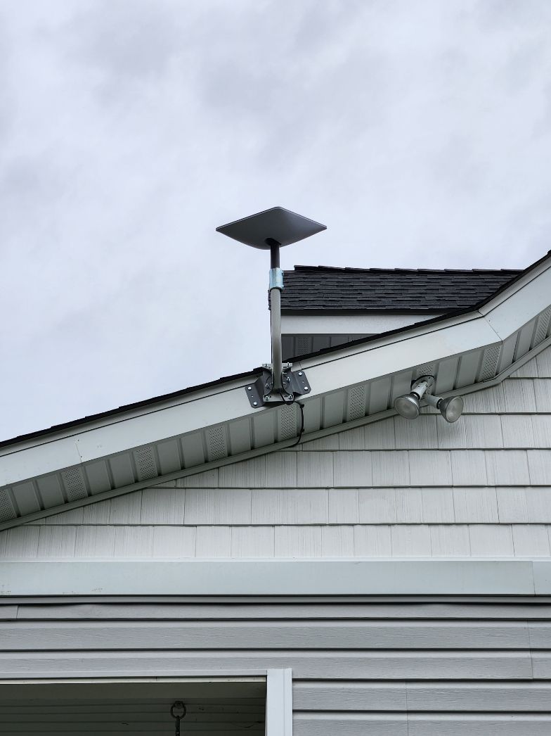 Small rooftop antenna mounted on a house roof against a cloudy sky