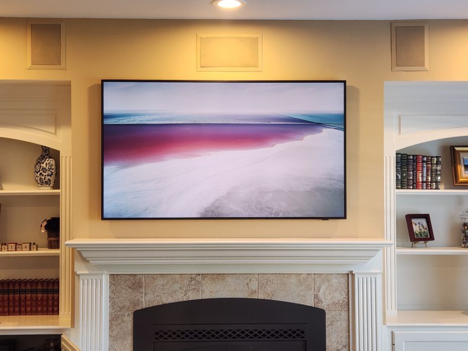 Wall-mounted TV above a fireplace in a cozy living room, displaying a pink beach scene