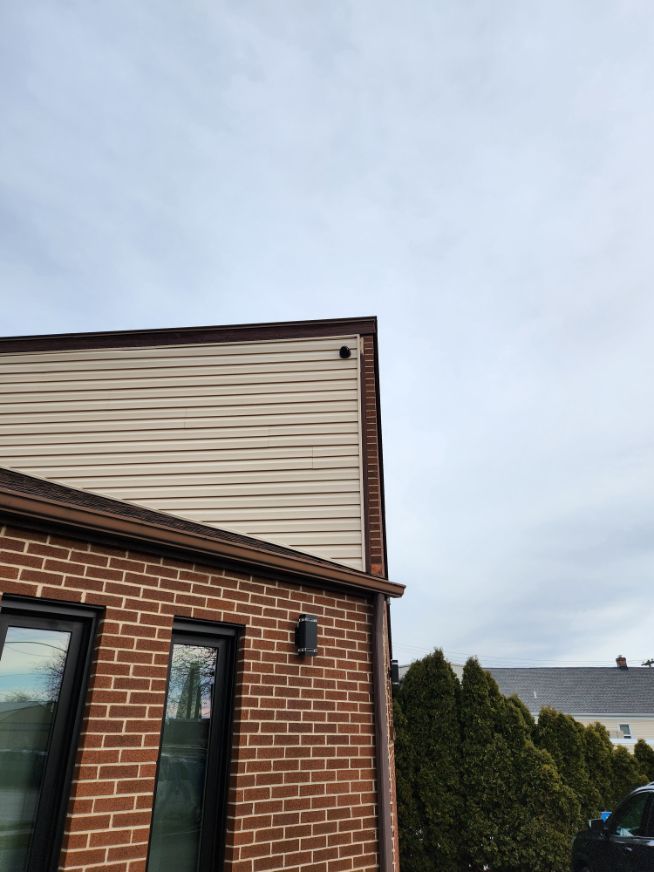 Brick house exterior with tan siding and a small dark green door under a cloudy sky