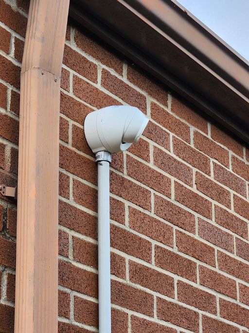 White vent cap and conduit on a red brick exterior wall near a roofline