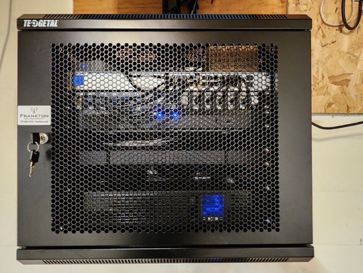 Black mesh cabinet on a shelf, showing electronic equipment and blue indicator lights inside.