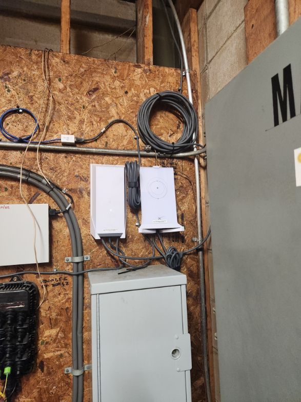 Electrical boxes and coiled cables mounted on a plywood wall beside a gray cabinet.
