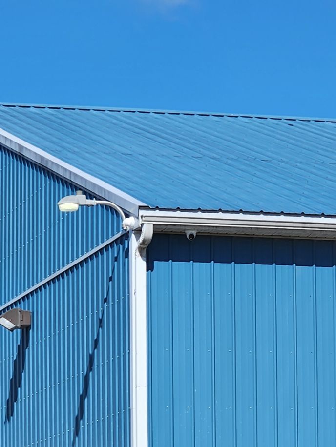 Blue industrial building with corrugated metal siding and roof under a clear blue sky, with a streetlight attached.