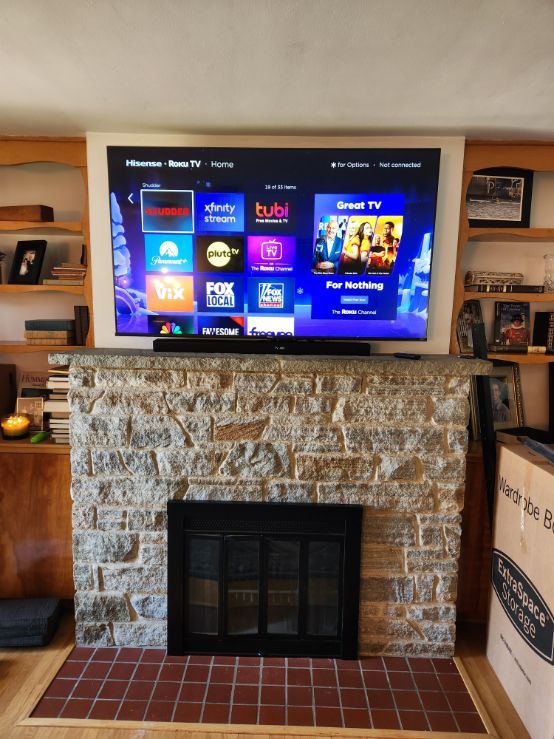 TV mounted above a stone fireplace with a streaming app menu displayed in a cozy living room