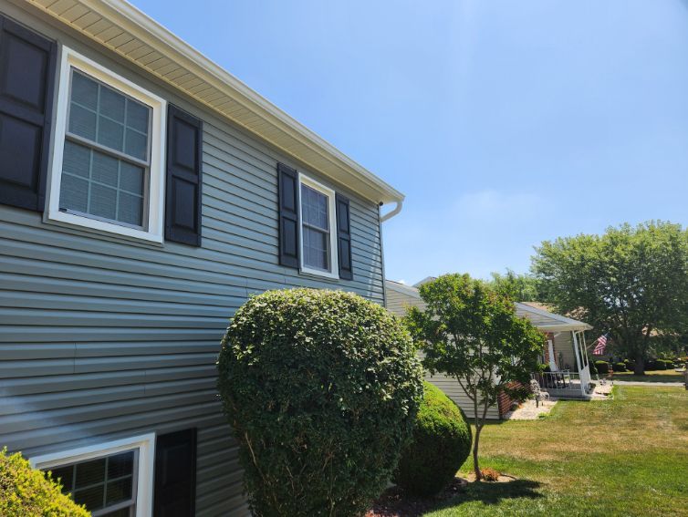 Suburban house with blue siding, white-trimmed windows, and neatly trimmed bushes on a sunny day