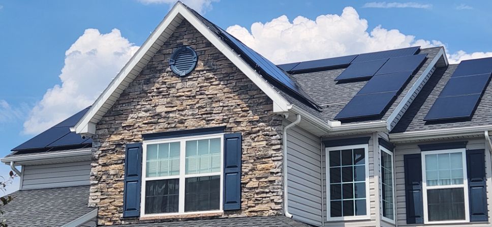 Stone-faced house with dark roof and solar panels under a blue sky