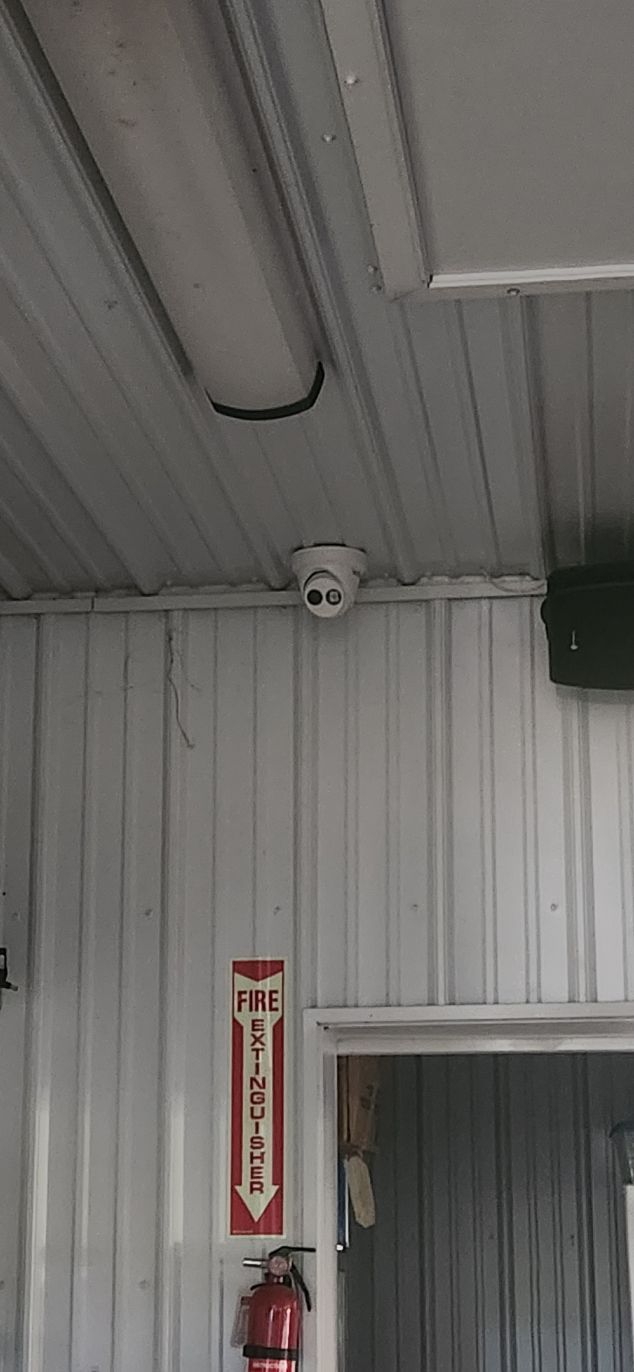 Indoor ceiling and doorway in a white corrugated-metal room, with a wall-mounted sign and security camera.