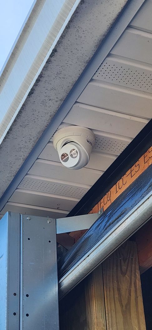 White security camera mounted under a roof eave above a doorway with a blue awning