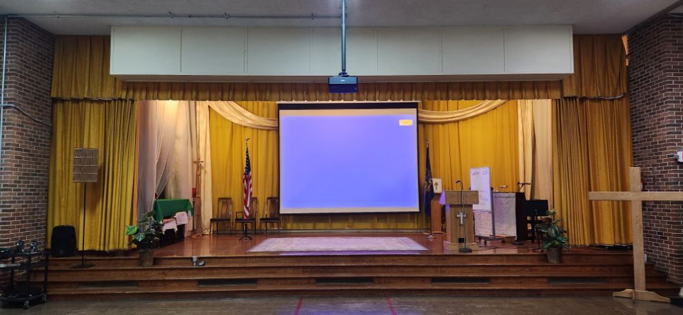 Empty stage with a blue projection screen, wooden backdrop, and steps in an auditorium