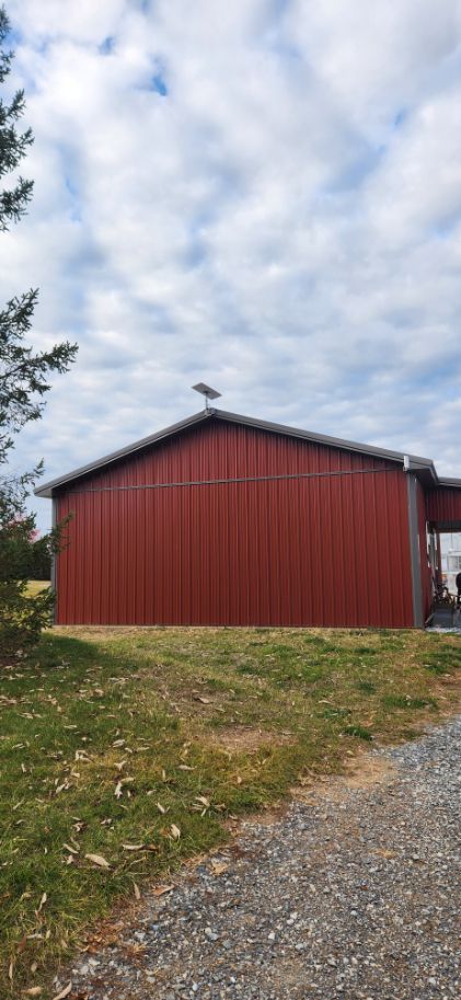 Red barn with a metal roof on a grassy slope beside a gravel path under a cloudy sky.