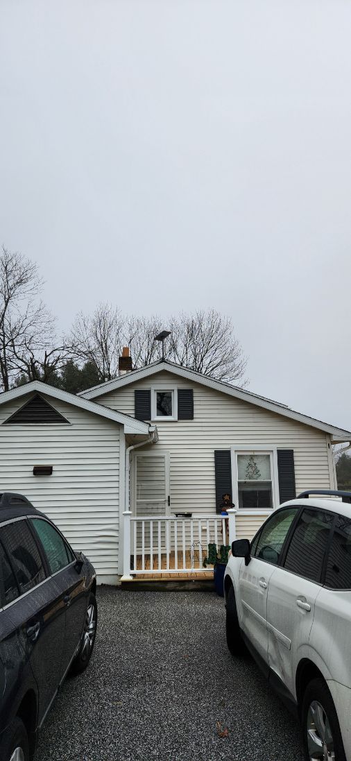 Single-story white house with a front porch, viewed between parked cars on a cloudy day