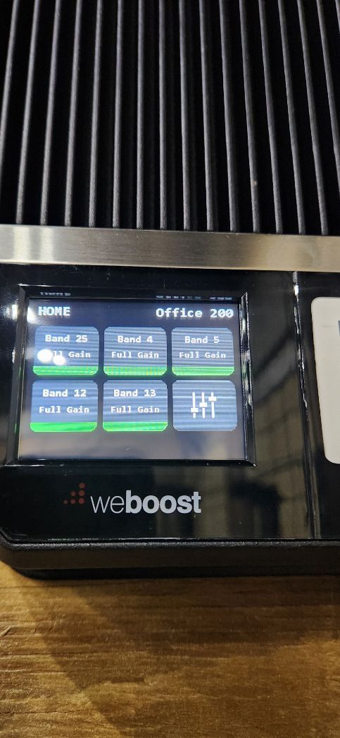 WeBoost signal booster with lit status screen and ribbed black front panel on a wooden table
