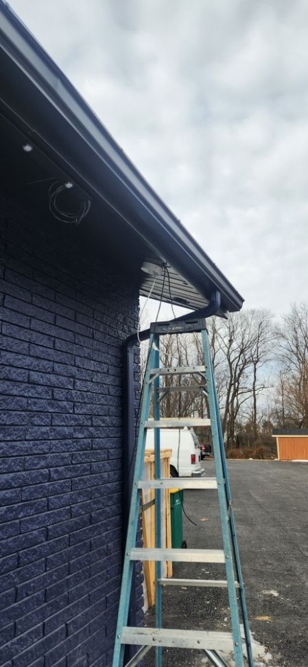 White ladder leaning against a dark blue house under the eaves beside a gravel driveway