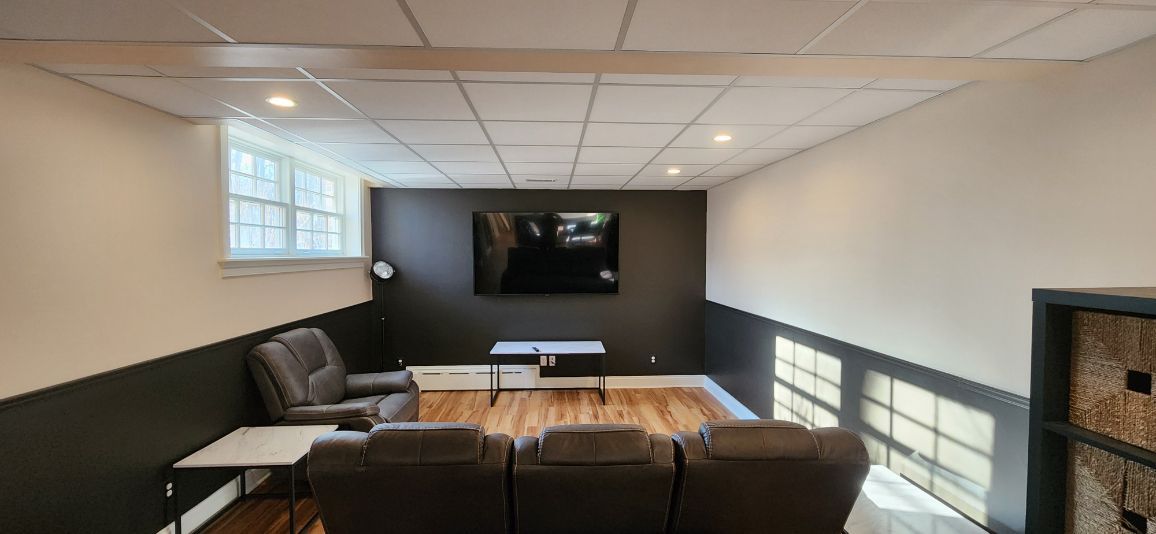 Modern basement lounge with sectional sofa, TV on dark wall, and bright windows along one side