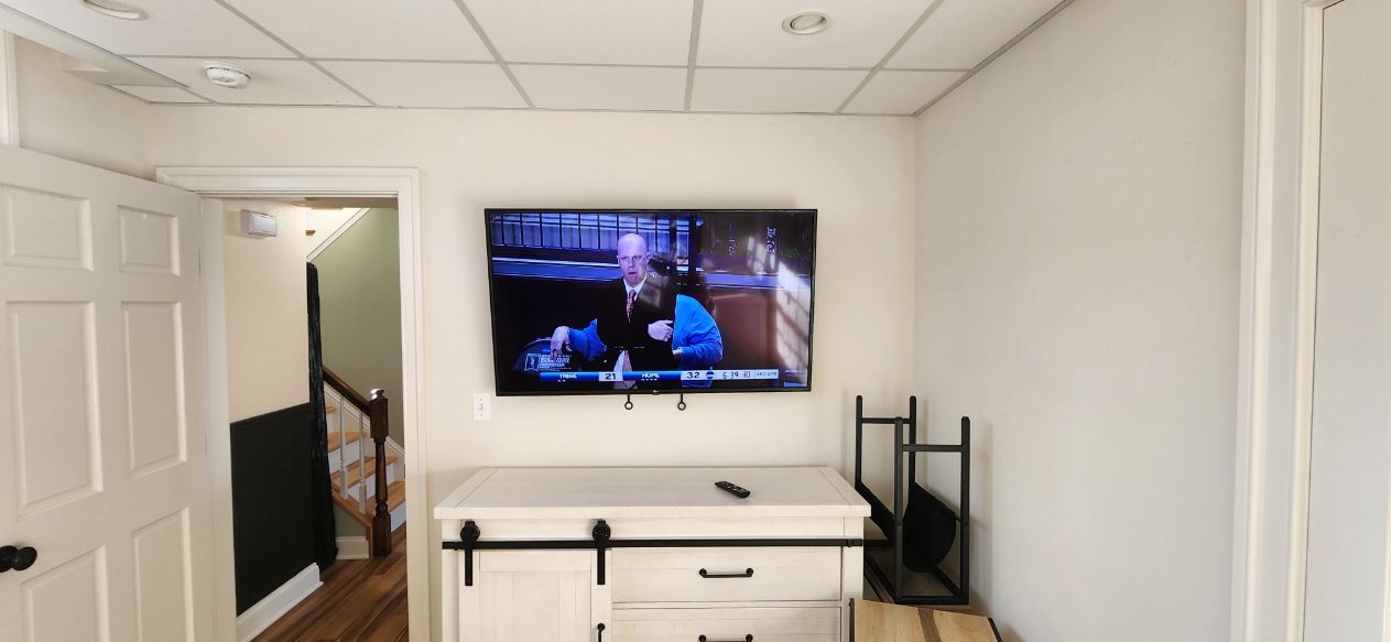 Bright white hallway with a wall-mounted TV above a white dresser and black shelving unit.