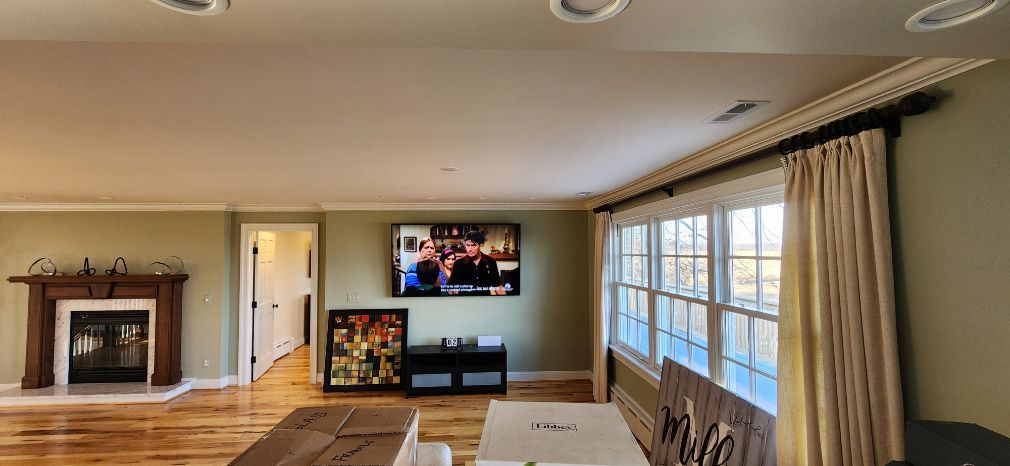 Bright living room with fireplace, wall-mounted TV, large window, and hardwood floor