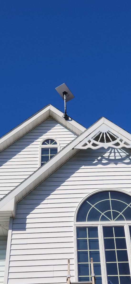 White house gable with decorative trim and arched window against a bright blue sky