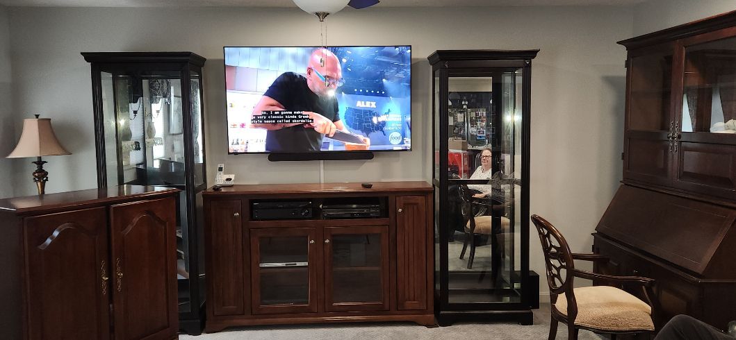 Living room with a wall-mounted TV, dark wood cabinets, glass display cases, and a brown chair.