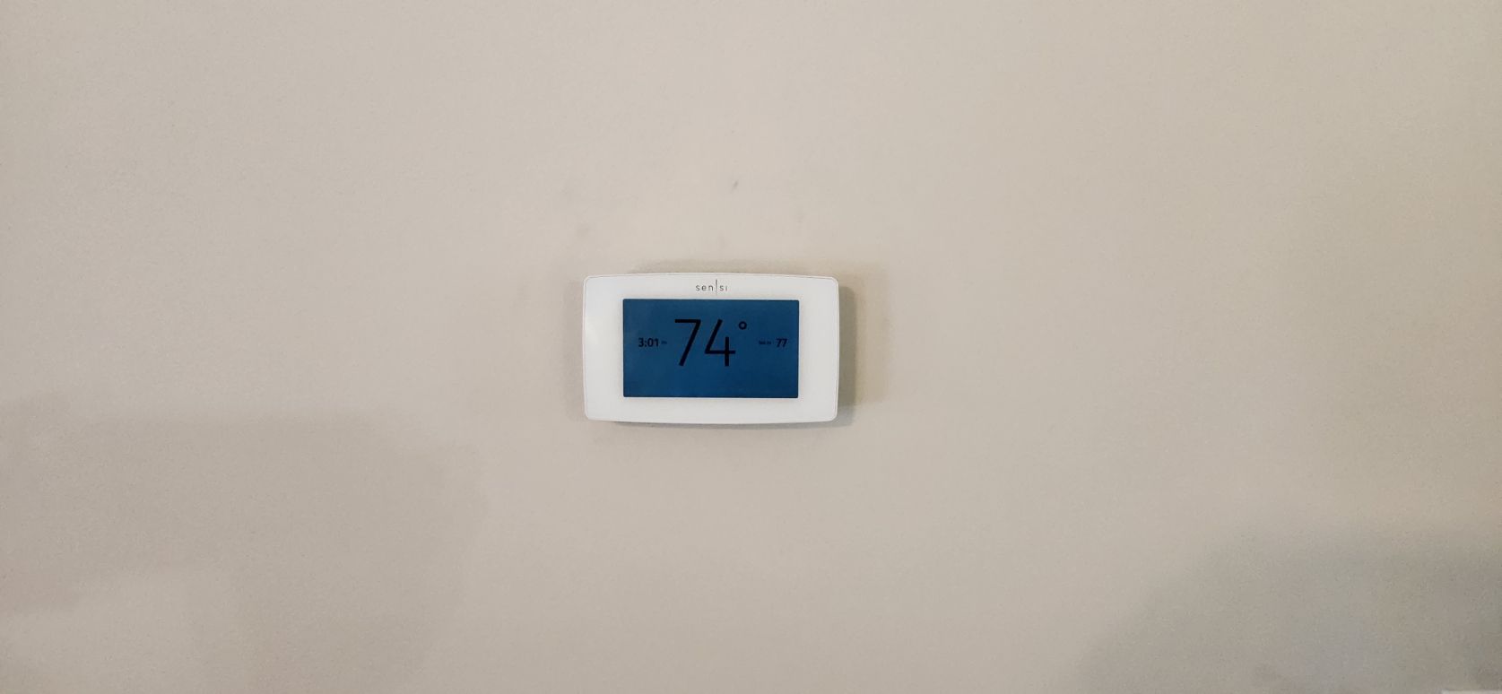 Small white wall-mounted thermostat with a blue digital display on a beige wall.