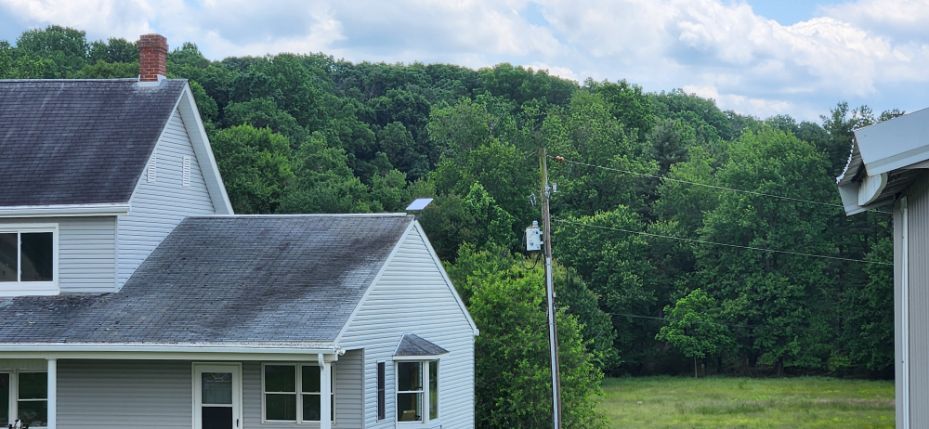 White houses by a green field and wooded hill under a cloudy blue sky