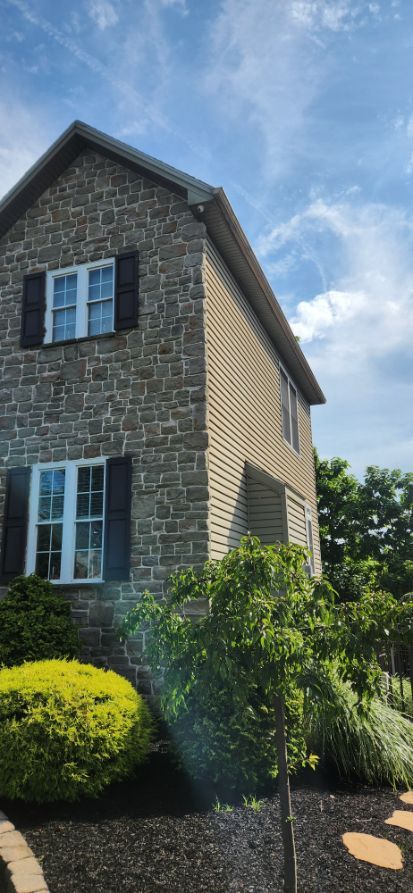 Stone house exterior with blue shutters, tan siding, and greenery under a clear sky