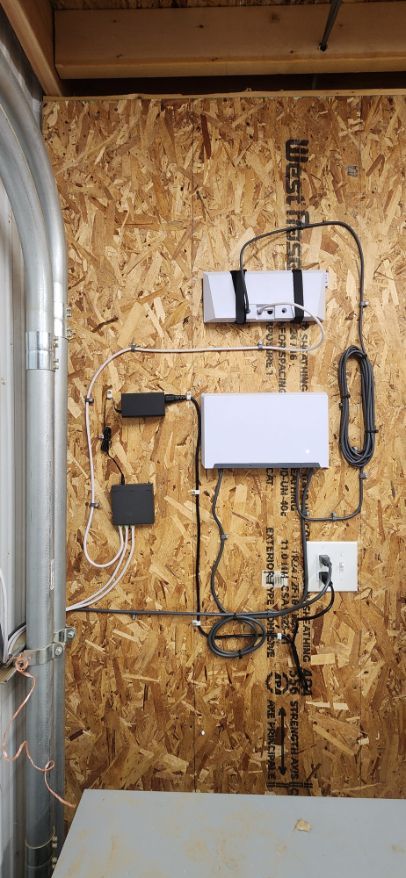 Wall-mounted electronics and cables on an OSB workshop wall, including boxes, conduit, and a power outlet.