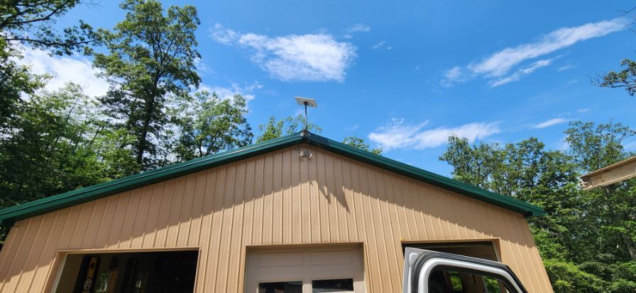 Tan tan house with green-trimmed roof under a blue sky, trees in the background.