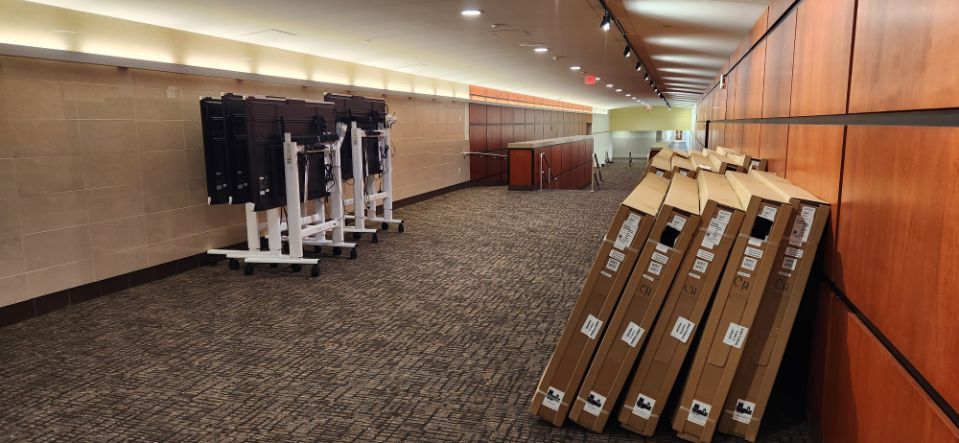 Empty hallway with stacked foldable tables and equipment carts along wood-paneled walls