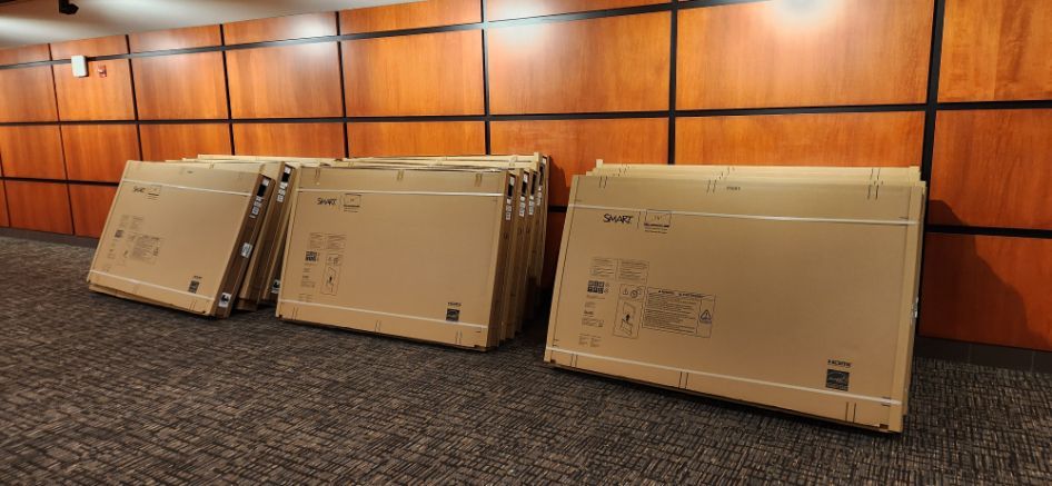 Three cardboard shipping boxes leaning against a wood-paneled wall on a carpeted floor.