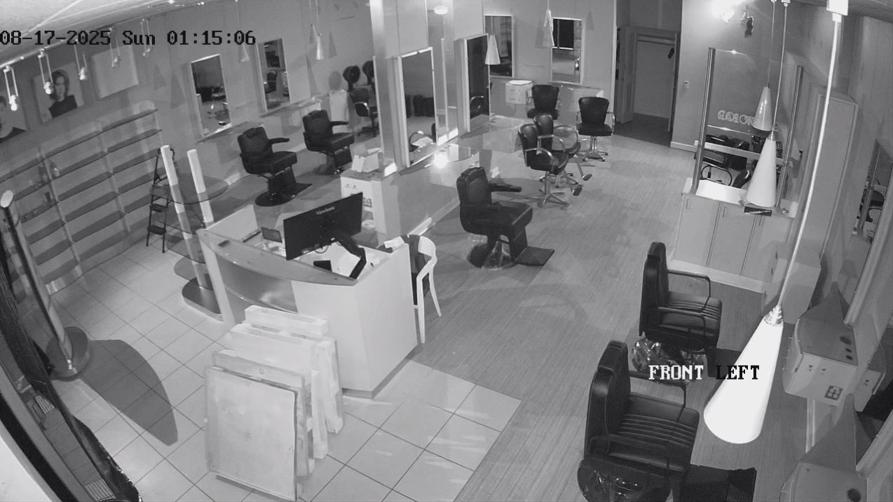 Surveillance view of a hair salon with people seated at styling stations and mirrors along the walls