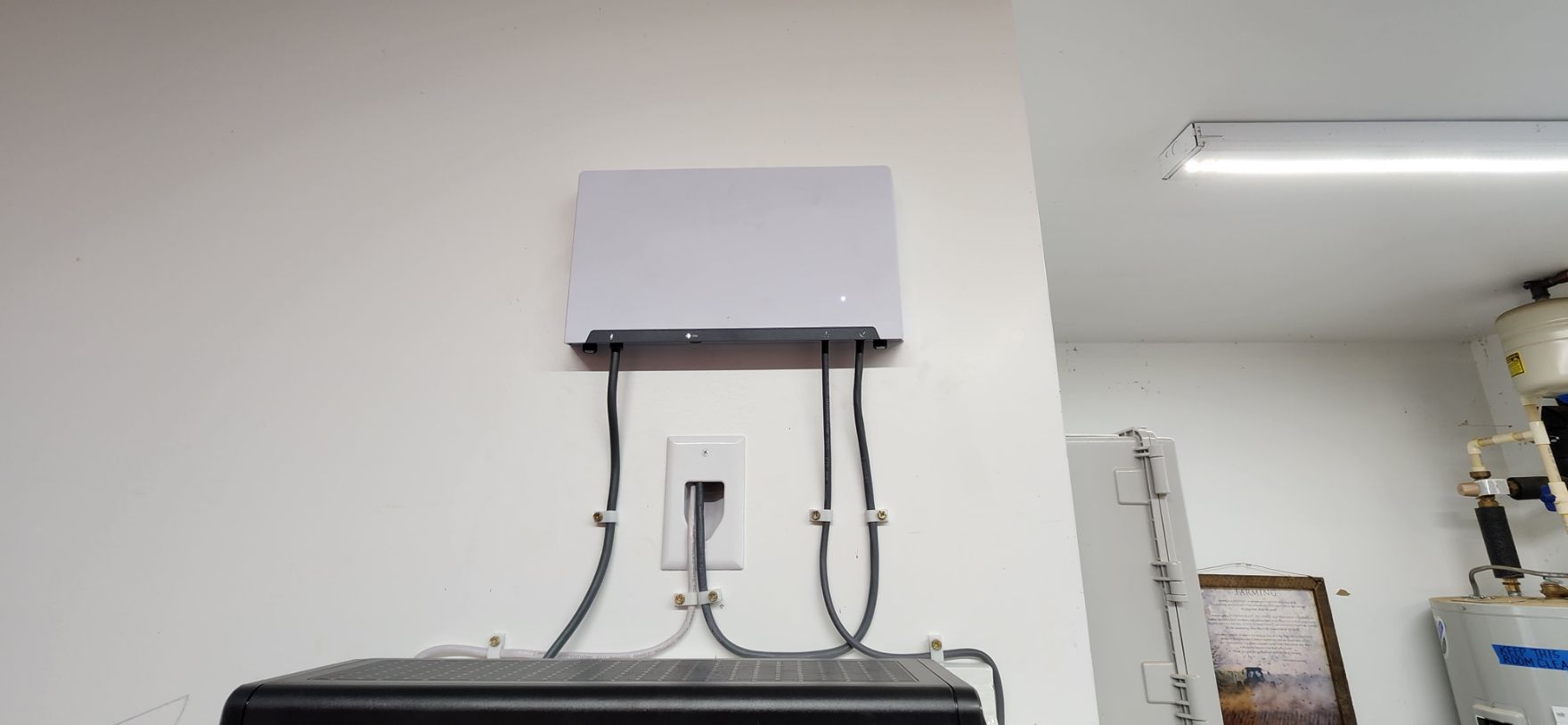 Wall-mounted white device with cables above a black cabinet in a bright room