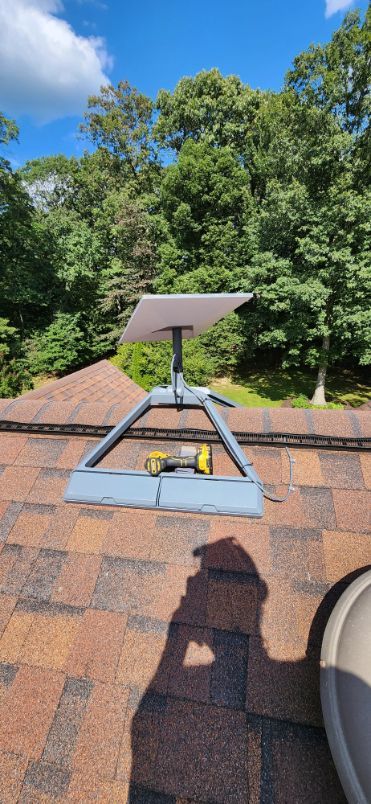 Solar panel mounted on a rooftop against a blue sky and green trees