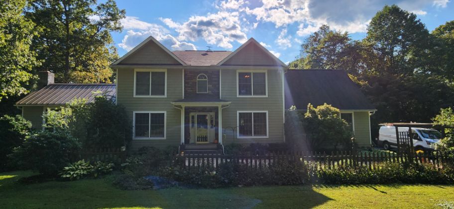 Two-story gray house with a porch and green yard in bright sunlight