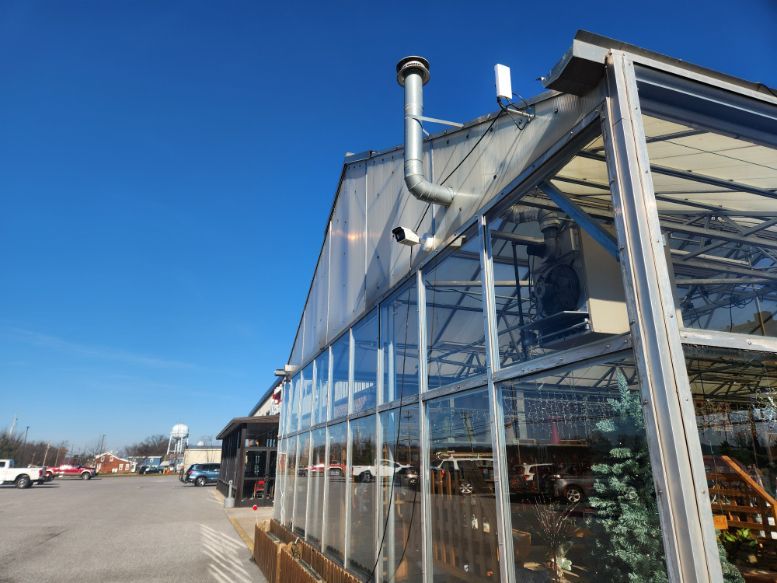 Glass greenhouse beside a parking lot under a clear blue sky