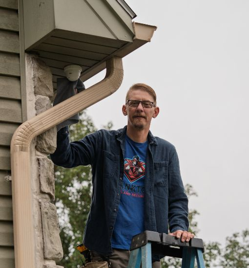 Man standing on a ladder painting the exterior trim of a house with a brush