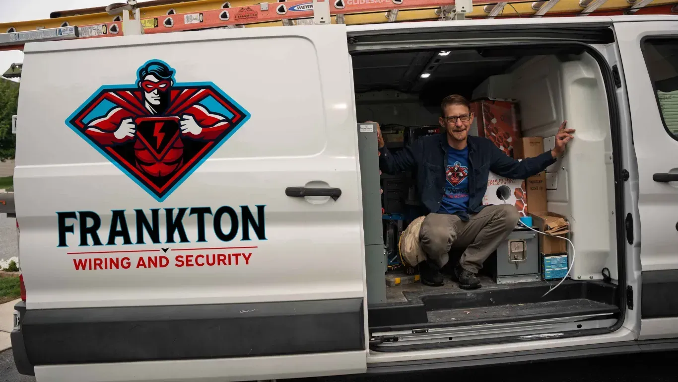 White work van with “FRANKTON Wiring and Security” logo; a man sits inside holding the open side door.