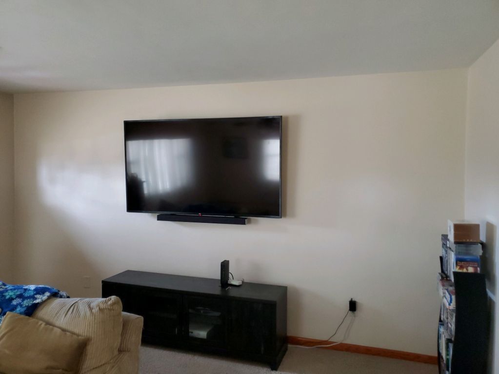 Living room with wall-mounted TV, black console, beige couch, and bookshelf in a bright corner.