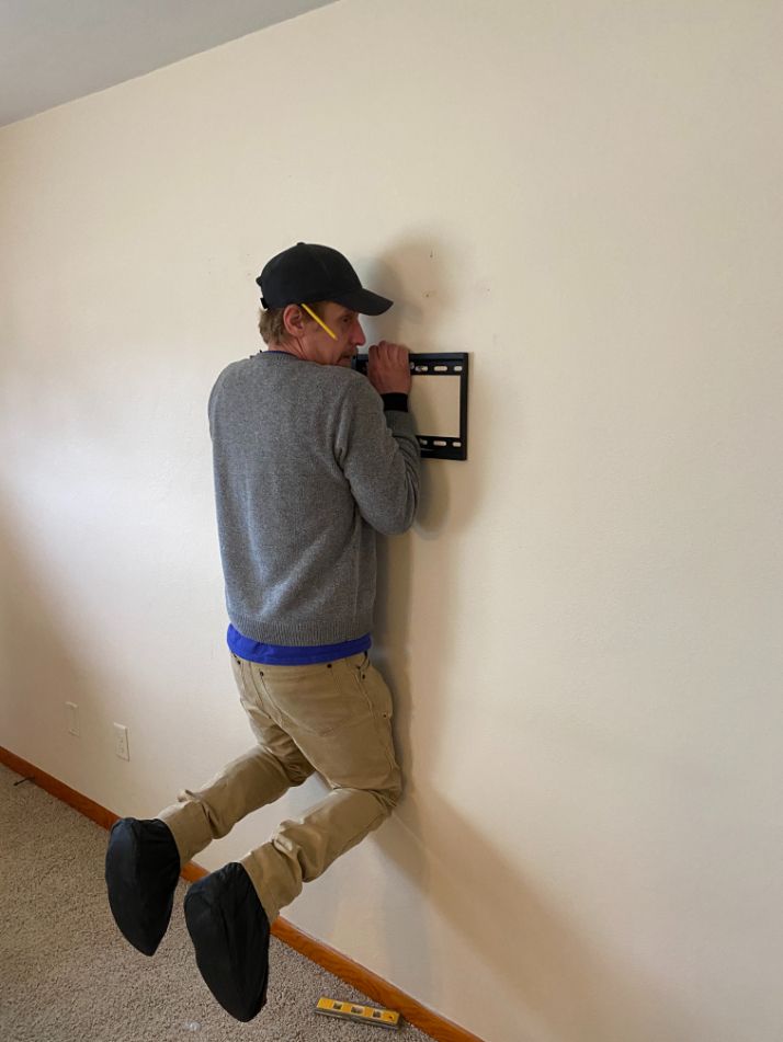 Person hanging against a wall, reaching toward a mounted panel in a hallway.
